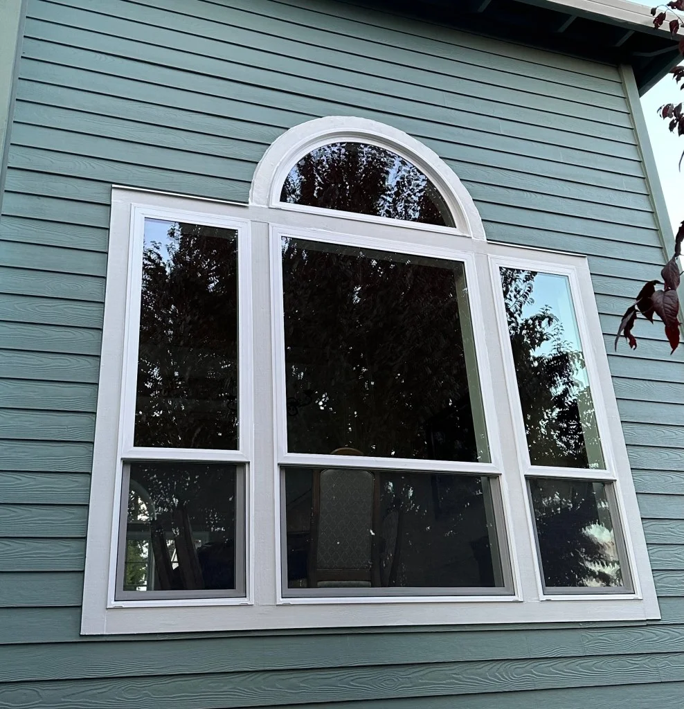 Large white-framed arched window with double-hung side units set into teal fiber-cement lap siding
