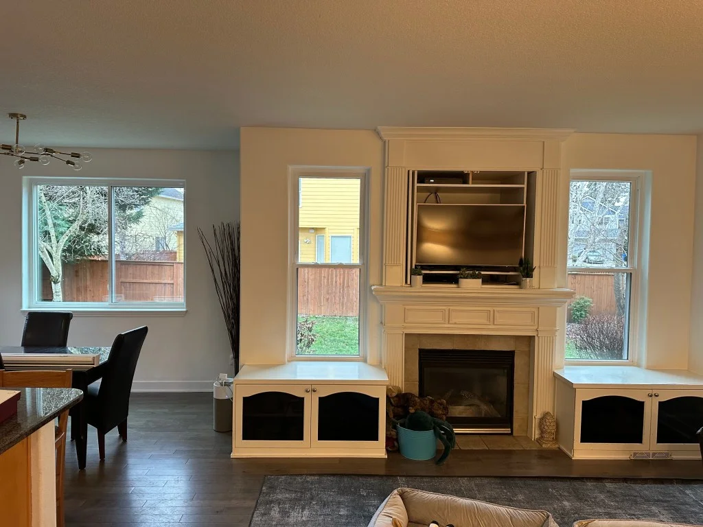 Living room with white double-hung windows flanking a white built-in fireplace and TV niche, with dark glass cabinets and hardwood floors