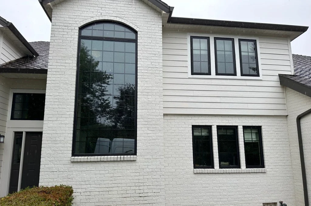 Two-story white brick home with arched black-framed grid window and black-framed grid windows on white lap siding