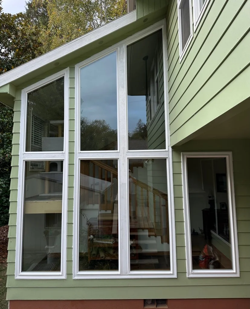 Tall white-framed multi-panel windows installed on green lap siding with a adjacent narrow window