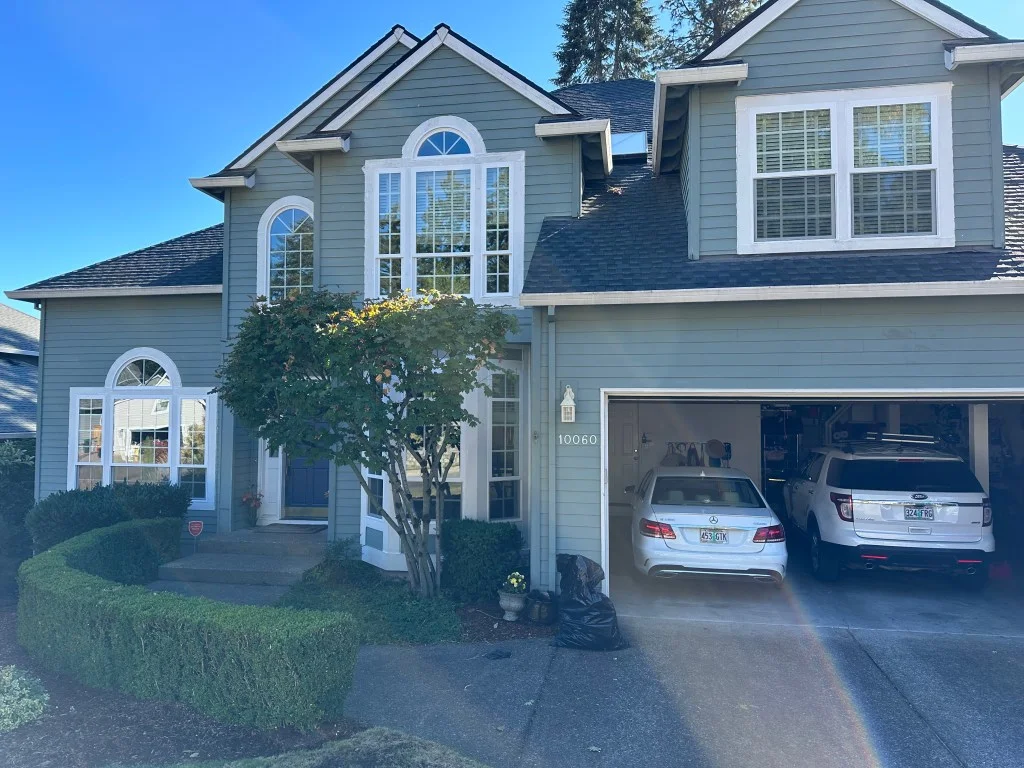 Two-story home with white-trimmed double-hung windows and arched-top windows over sage green lap siding and gray shingle roof